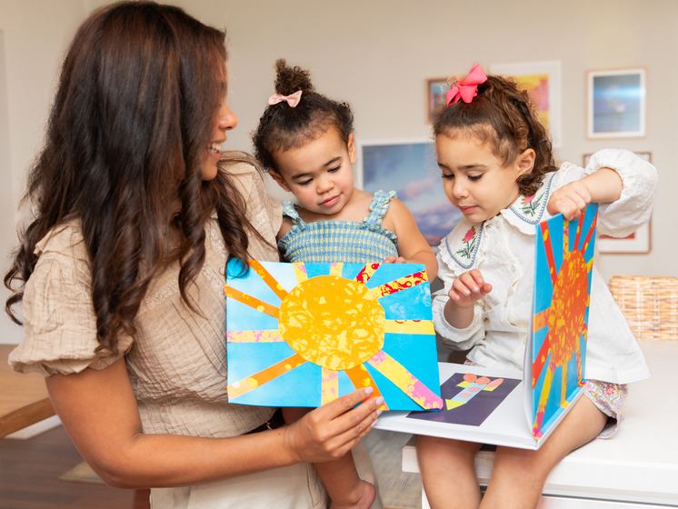 A mom and her two kids on the couch holding up a rainbow painting
