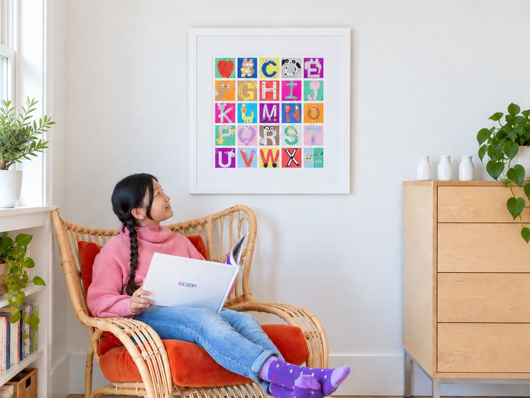 A girl reading in a chair under a framed mosaic in a playroom
